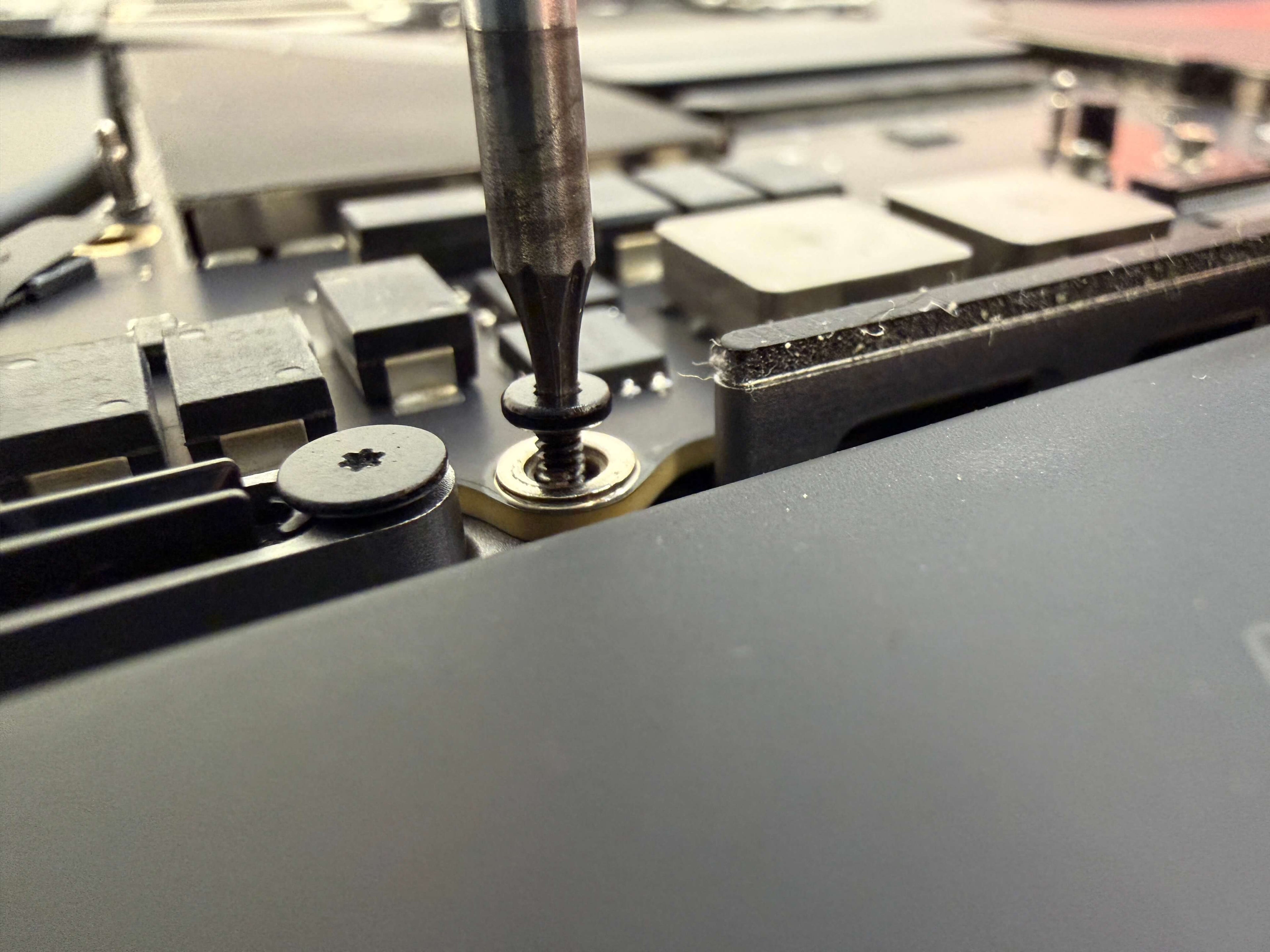 Close up of a screwdriver removing a T5 screw from the logic board of a MacBook